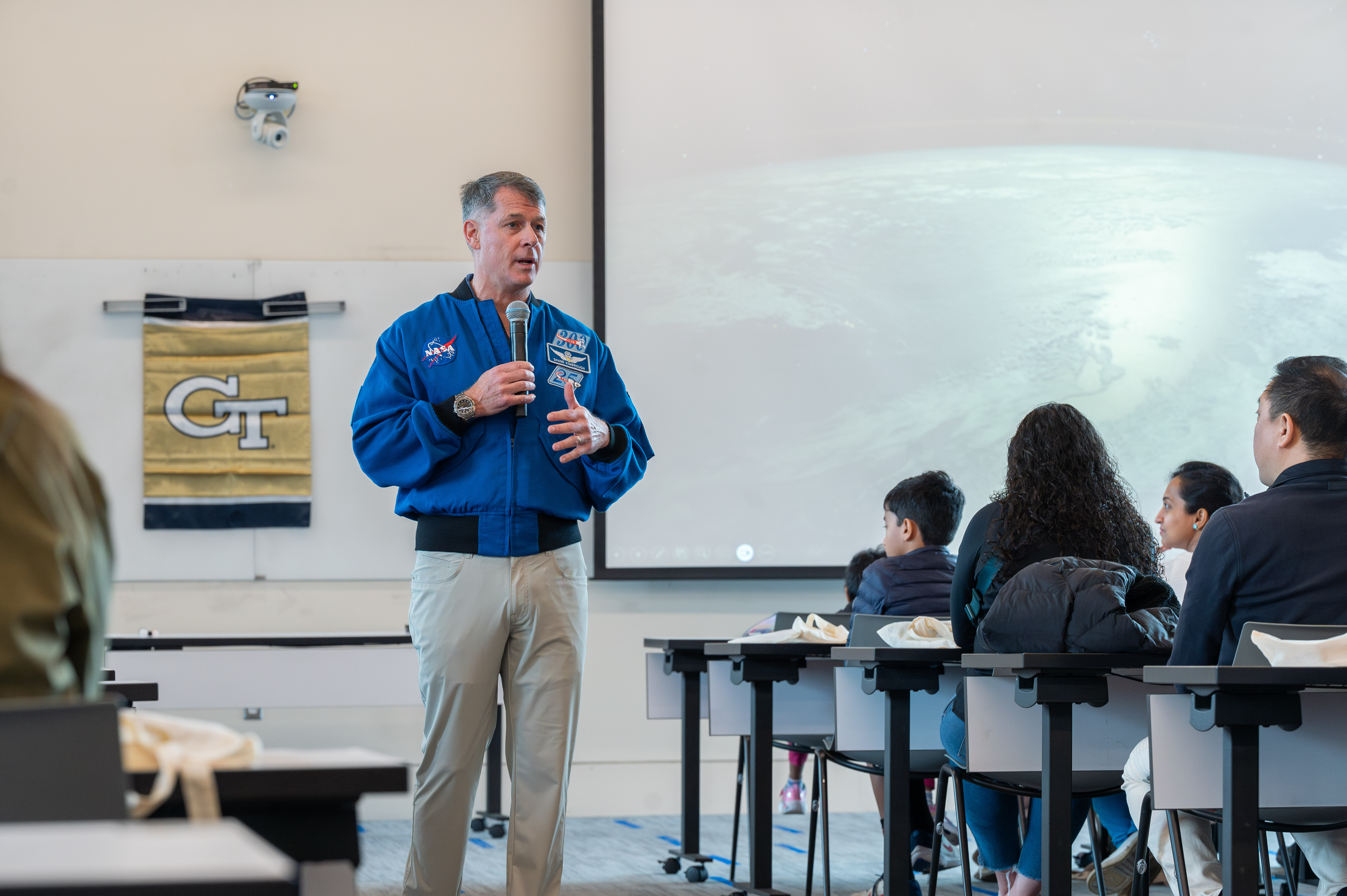 A man in a blue shirt stands in front of a class of adolescents