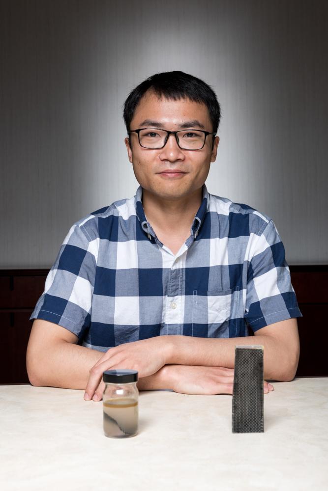 <p>Kai Yu, a former postdoctoral researcher in The George W. Woodruff School of Mechanical Engineering at Georgia Tec, sits behind a piece of carbon fiber composite immersed in alcohol. (Credit: Rob Felt, Georgia Tech)</p>