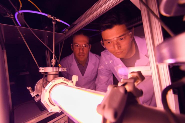 <p>Georgia Tech Professor Lukas Graber and Postdoctoral Fellow Chanyeop Park study the plasma potential surrounding materials being evaluated for use in improved DC circuit breakers. The low-energy argon plasma creates the purple color. (Photo: Rob Felt, Georgia Tech)</p>