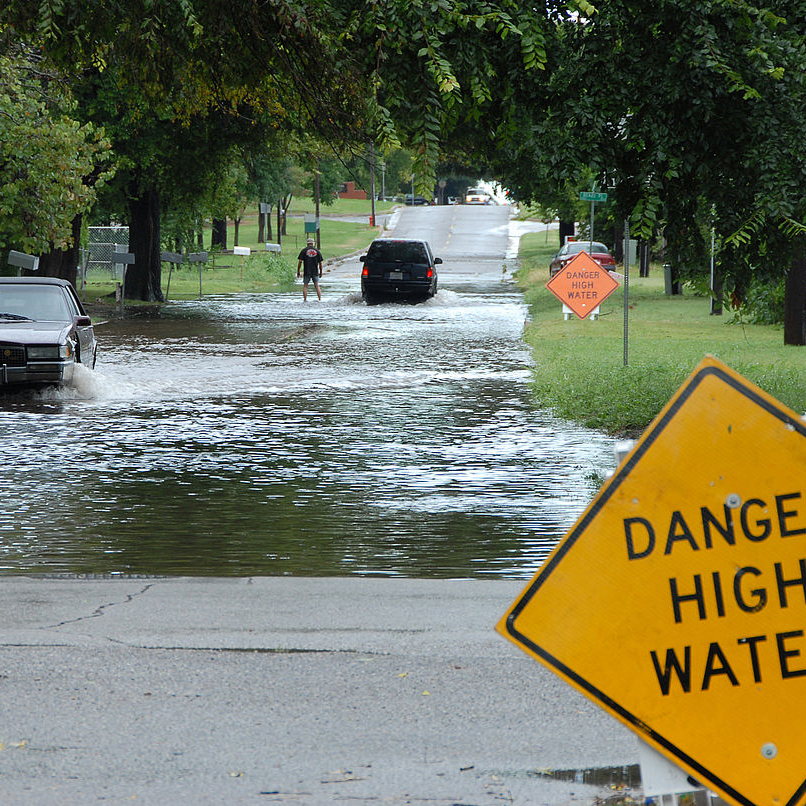 A car drives through a flooded section of a neighborhood street.