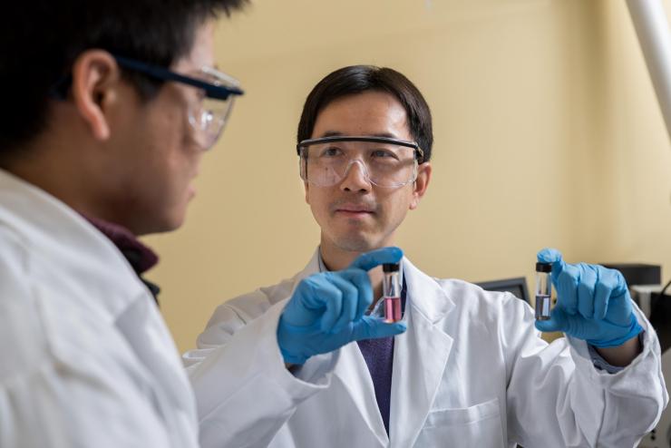 <p>Georgia Tech Professor Zhiqun Lin and Postdoctoral Fellow Yihuang Chen discuss samples of hairy nanoparticles made with light-sensitive materials that assemble themselves with light exposure. The nanoparticles could one day become “nano-carriers” providing doctors a new way to simultaneously introduce both therapeutic drugs and cancer-fighting heat into tumors. (Credit: Rob Felt, Georgia Tech)</p>