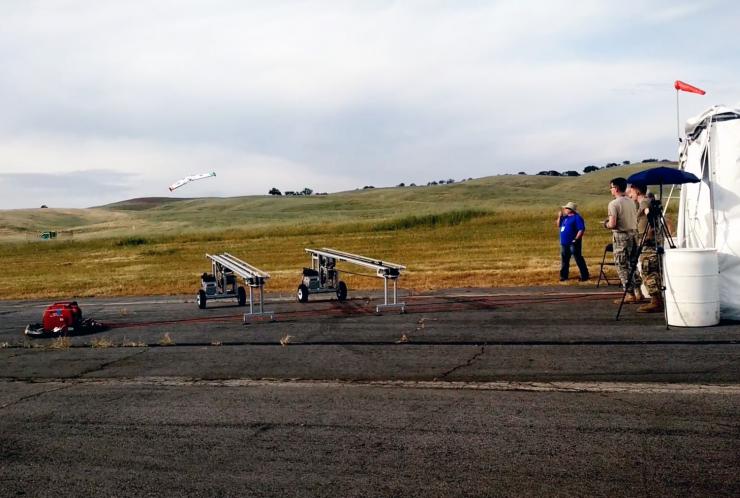 <p>A service academy team watches as one of its fixed-wing aircraft flies after launch. (Credit: DARPA)</p>