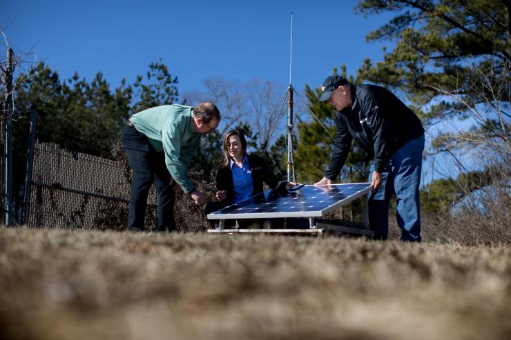 <p>John Trostel, director of the Severe Storms Research Center (SSRC), Madeline Frank, a research meteorologist at the SSRC, and Tom Perry, an SSRC electrical engineer, examine equipment for the North Georgia Lightning Mapping Array, a network of 12 sensors located around the metropolitan Atlanta area to detect lightning that may indicate storm intensification. (Credit: Branden Camp, Georgia Tech Research Institute)</p>