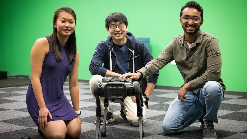 Three students kneeling around a spot robot