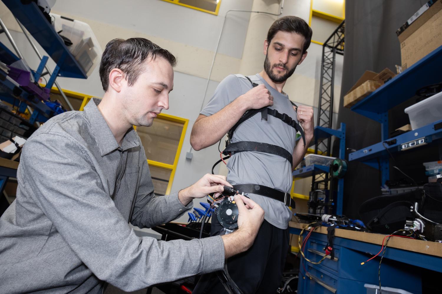 two people in the lab make adjustments to a robotic exoskeleton