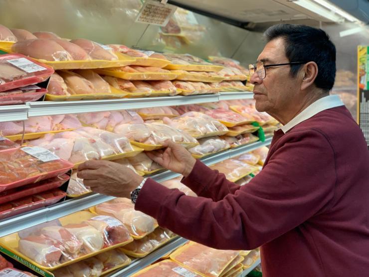 A man in a crimson colored sweater peruses the meat cooler in a supermarket.