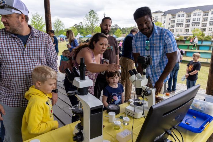 <p><em>A group looking through microscopes set up by GTRI volunteers at the Science Day in the Park (Photo Credit: Ethan Trewhitt). </em></p>