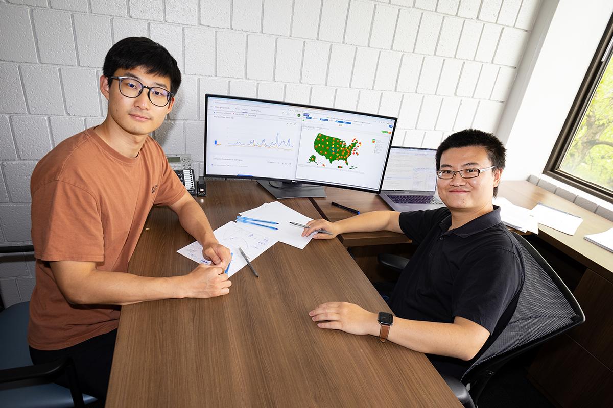 Ph.D student Simin Ma sits with Assistant Professor Shihao Yang at his desk. A computer monitor shows flu data and Google search trends that they used in their Covid and flu forecasting models.