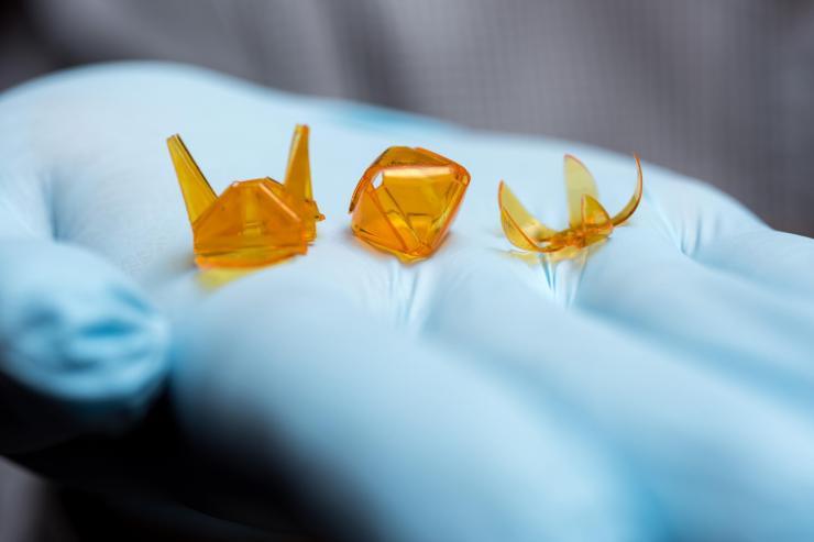 <p>A new technique for producing self-folding three-dimensional origami structures from photo-curable liquid polymer materials created these tiny samples, held in a hand for size comparison. (Credit: Rob Felt, Georgia Tech)</p>