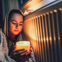 A young girl wrapped in a blanket holds a candle during a power outage.